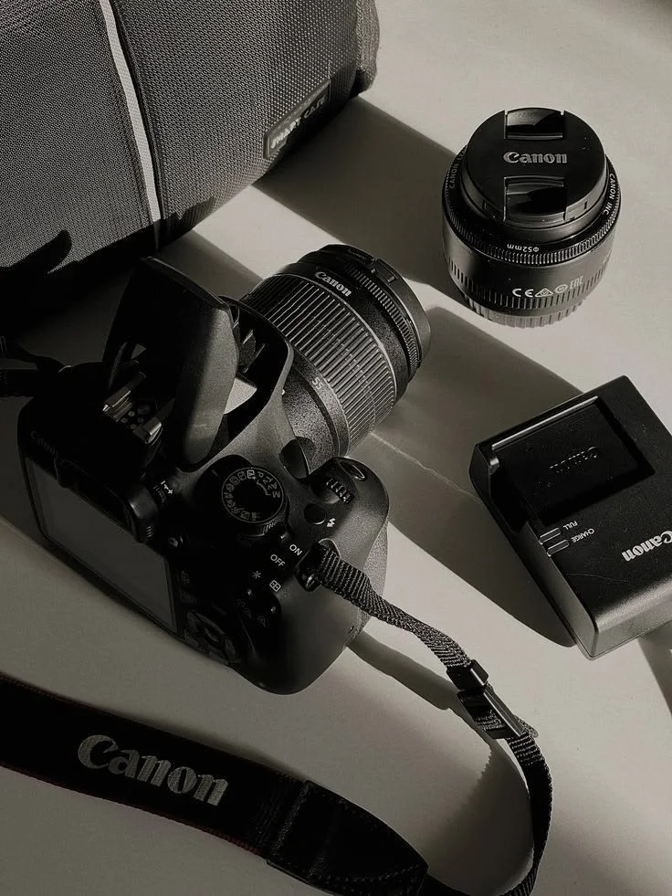 Câmera Canon, lentes e carregador sobre a mesa